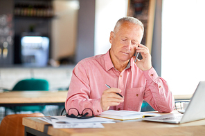 Contemporary senior businessman with smartphone consulting client or talking to business partner at work