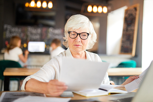 Mature economist reading financial papers while working by table in cafe