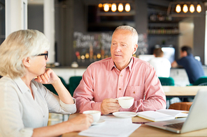 Two senior economists having tea-break in cafe and discussing some working points or ideas