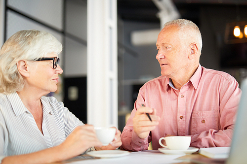 Two senior employees sitting in cafe and having working conversation by cup of tea