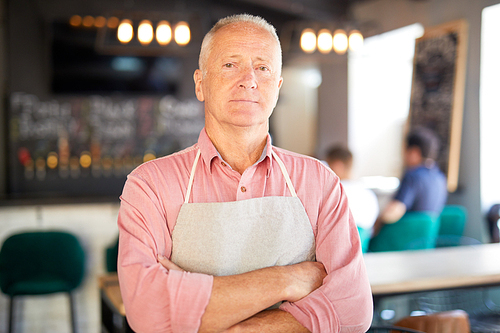 Senior owner of cafe in workwear crossing his arms on chest while looking at you