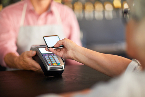 Modern visitor paying through mobile payment system in smartphone after eating in cafe