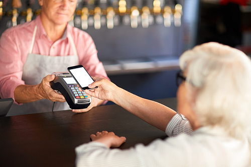 Modern senior woman holding her smartphone over payment machine held by waiter