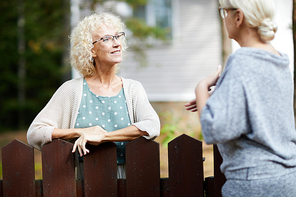 Two mature female neighbours talking through fence about everyday life stuff