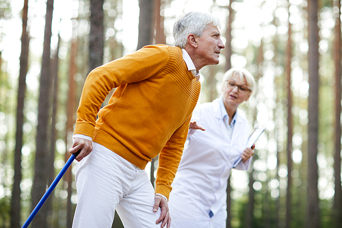 Senior man with cane limping while walking to hospital for medical help with nurse near by