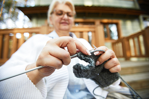 Hands of grandma knitting grey woolen clothes for her family while relaxing outdoors