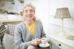 Happy blond mature woman with cup of tea  while having home rest