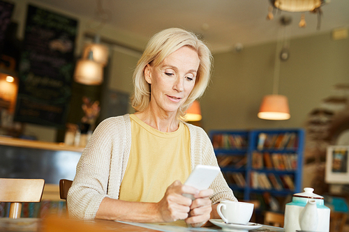 Blonde mobile woman sitting in cafe and reading sms or texting in smartphone