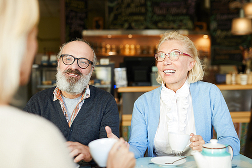 Aged couple talking to their friend by cup of tea during discussion of curious news in cafe