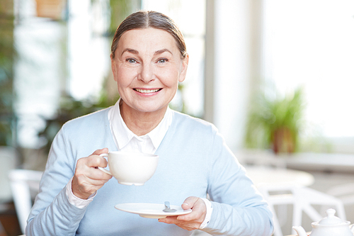 Pretty senior female with cup of tea or coffee having rest or coffee-break in cafe