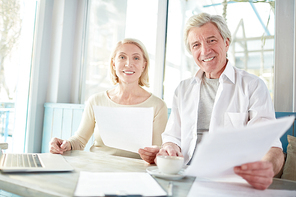 Smiling businessman and his pretty colleague with papers having meeting in cafe