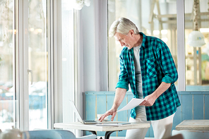 Senior man in casualwear looking through online information while preparing for report