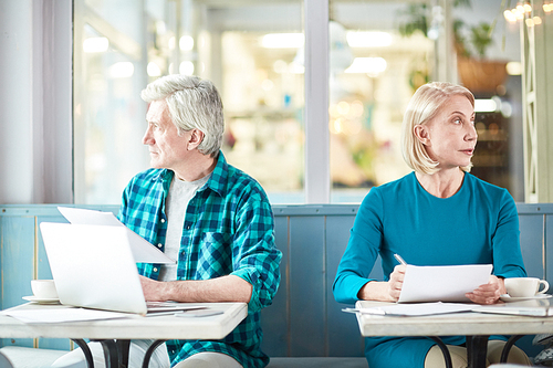 Pensive mature colleagues with papers working individually while sitting in cafe