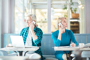 Two professionals with smartphones calling clients or subordinates while working in cafe