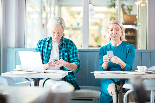 Mature man and woman texting or reading messages in their smartphones while sitting in cafe