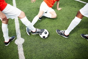 Legs of three young football players in long white socks and sneakers during game on green field