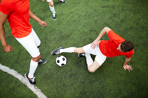 Top view of young player going to kick soccer ball while half lying on football field with his mate near by