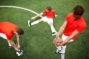 Three young soccer players in uniform exercising on green field before start of game