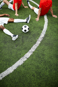 Group of tired or restful football players having break on green field before new game