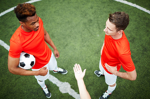 Two young footballers standing on green field opposite one another with open palm holding coin or chip between them