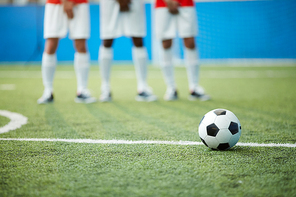 Soccer ball on green football field by dividing line and legs of three players on background