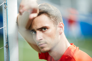 Young footballer or goalkeeper leaning against net while  after game