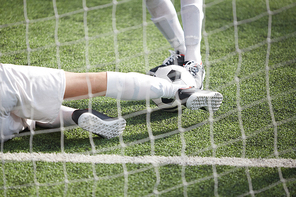 Legs of two footballers pursuing soccer ball during game on green field behind net