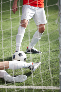 One of players kicking soccer ball in gates while goalkeeper trying to catch it