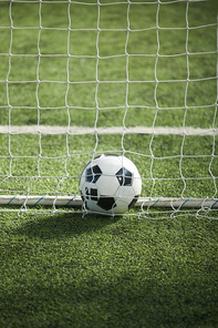 Soccer ball lying on green grass on empty football field behind net