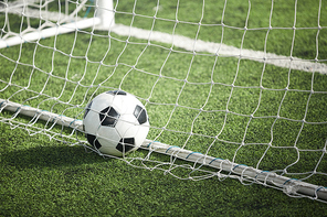 Leather soccer ball in empty gate behind net on green football field