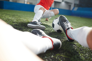 Legs of goalkeeper trying to push soccer ball and one of players lying in front of him