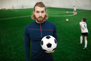 Young muscular sports trainer in activewear  while his team training on pitch