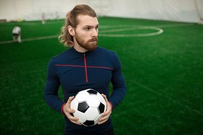 Active young football trainer in sportswear looking aside while standing on pitch