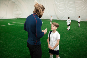 Youthful member of football team consulting with his trainer during game on pitch