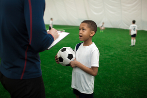 One of little players of football team with ball talking to his trainer after game