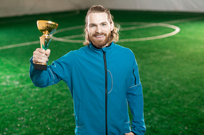 Young successful soccer player in activewear holding award on background of green football field