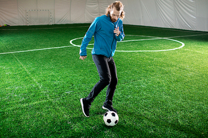 Young man in sportswear running before soccer ball on green pitch during training