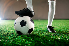 Young soccer player in boots and socks keeping one foot on ball while standing on green lawn