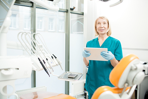 Confident dentist in gloves and uniform searching for information in the net before appointment with new patient