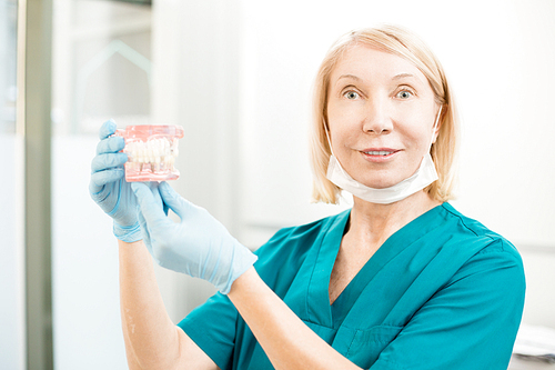 Contemporary dentist in uniform and gloves showing new false teeth and 