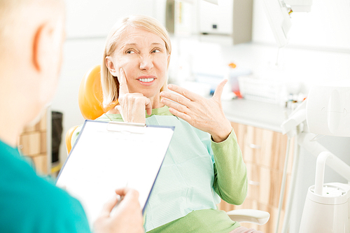 Mature patient complaining about pain in one of upper teeth during appointment with dentist