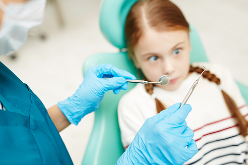 Close-up of unrecognizable dentist in surgical gloves holding scaler and mouth mirror and ready for checkup, scared child having dental phobia