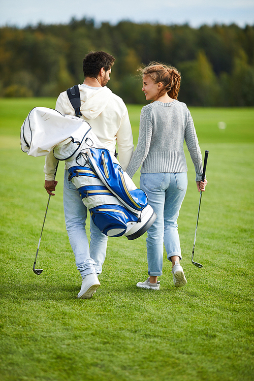 Rear view of young casual couple with golf equipment walking back home after play