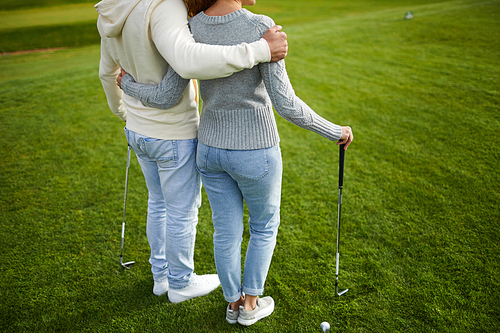 Two young casual golf players with clubs standing on green lawn before game