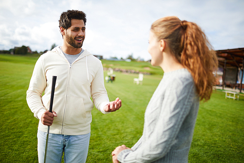 Young man in white hoodie and blue jeans explaining his girlfriend or golfer some play stuff