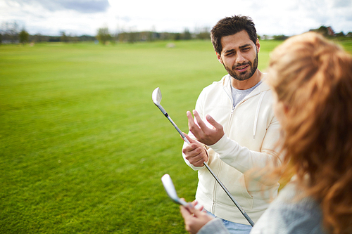 Active young man in casualwear having talk to his girlfriend while going to play golf on the field