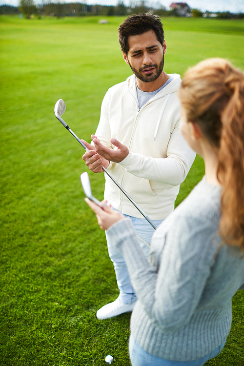 Confident young golfer with club explaining female how to choose right place for game