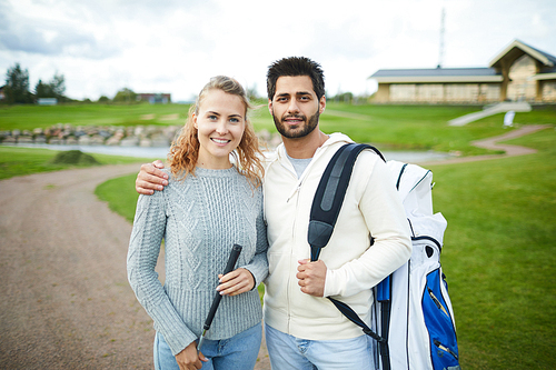 Happy young affectionate couple in casualwear going for golf play with equipment