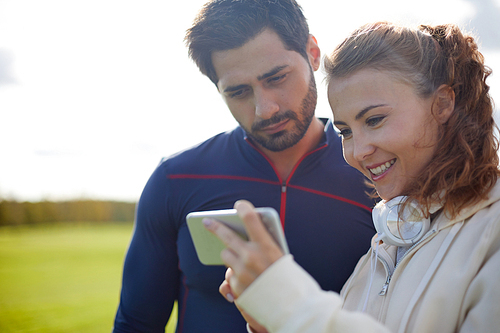 Young active couple watching curious stuff in smartphone of pretty girl outdoors