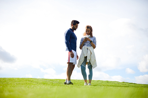 Young contemporary sporty couple standing on green field on summer day